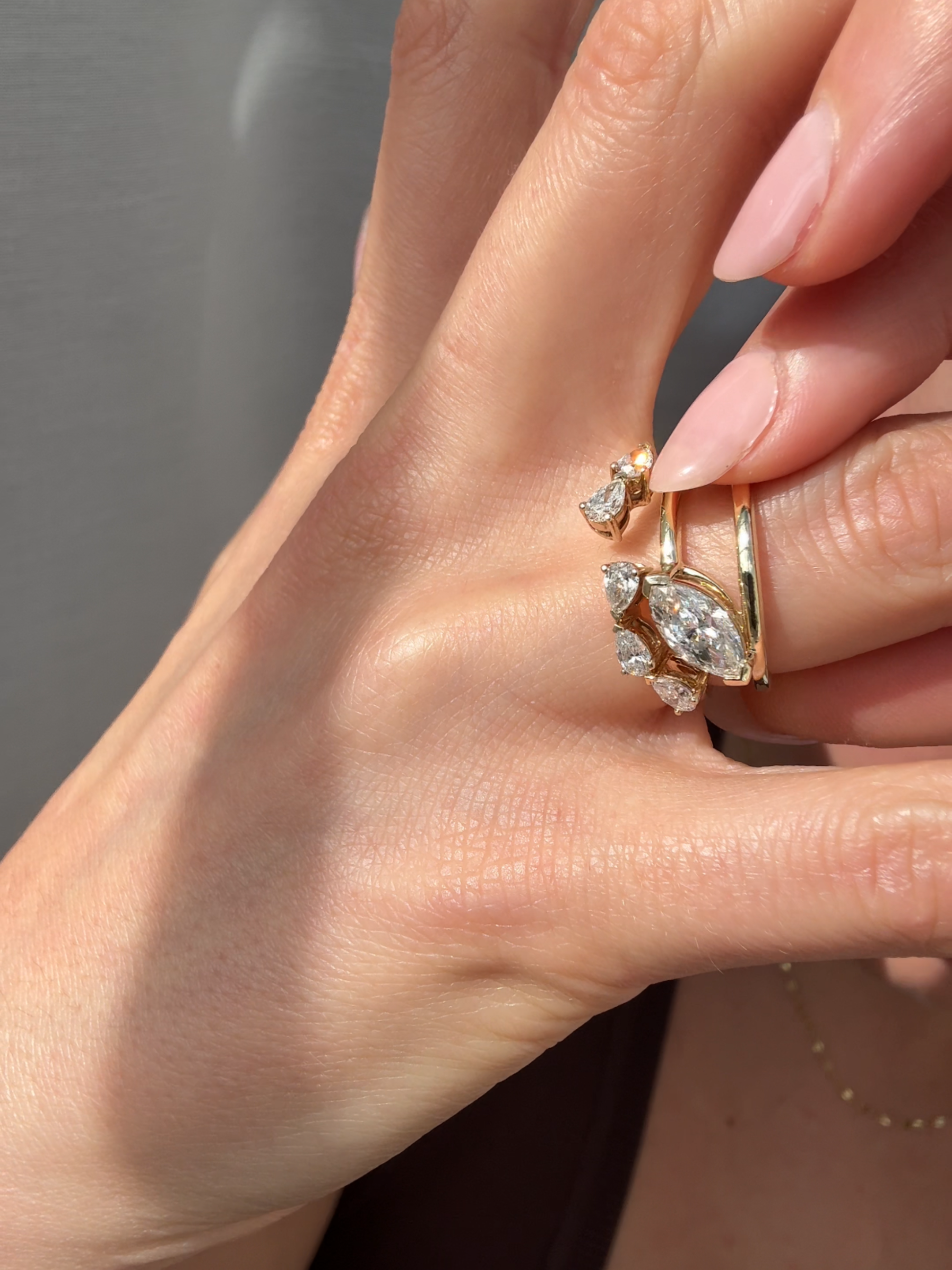 Hand wearing a gold rings with a diamond design against a neutral background