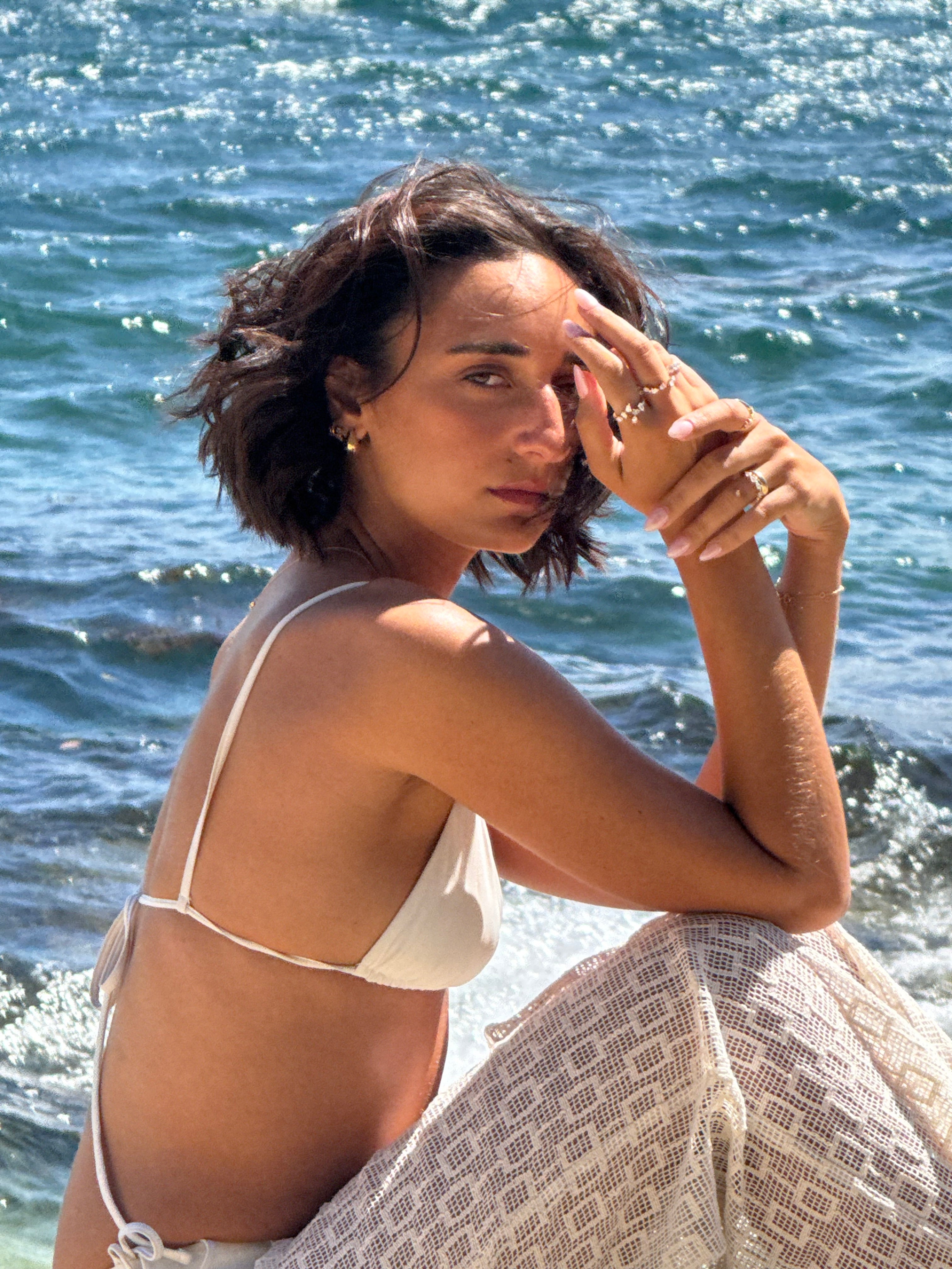 Woman in a white bikini standing by a body of water with diamond rings