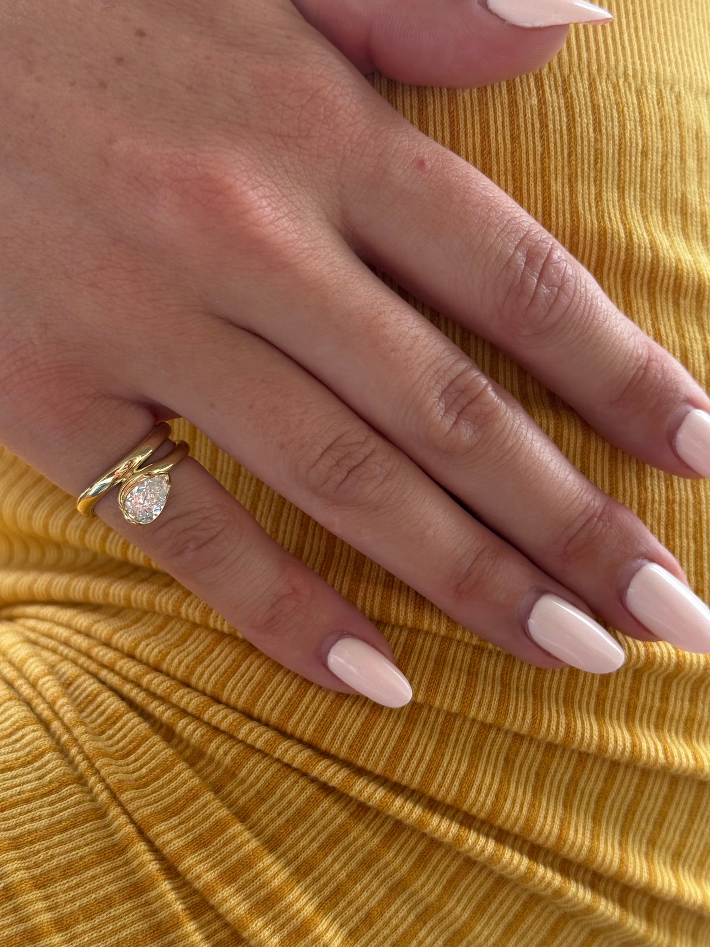 Side view of the GLO pinky ring showing a pear-cut white lab-grown diamond set east-west in a half-bezel scooped band
