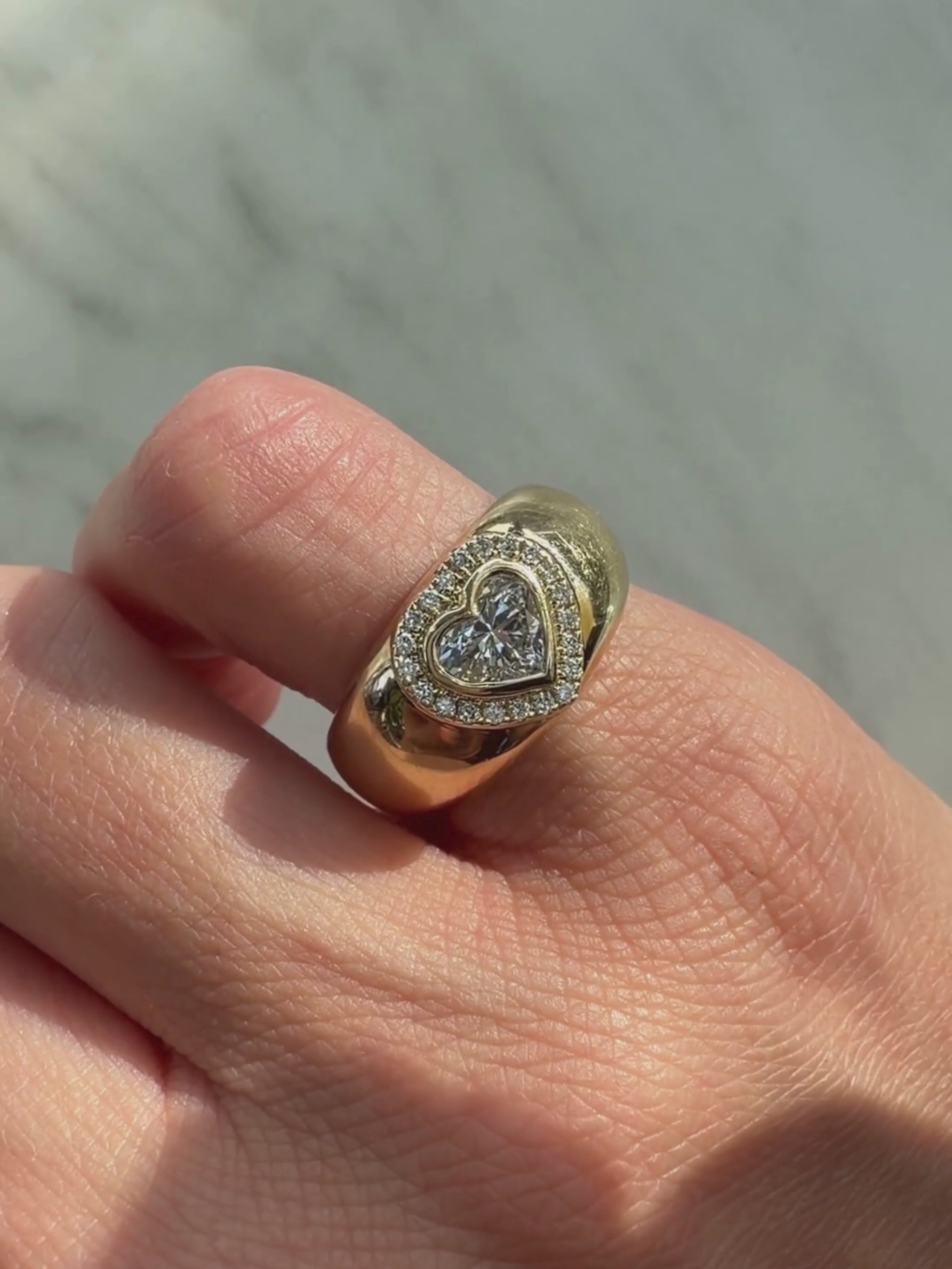 A video of Dina Halo gold heart signet in   a finger with white background